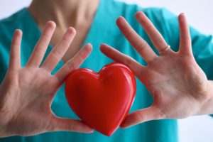 Nurse in turquoise scrubs holding a heart-shaped stress ball