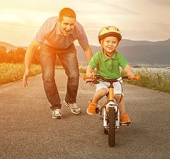 dad teaching child to ride bike