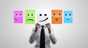 Person holding up different colored paper displaying emotions in front of face