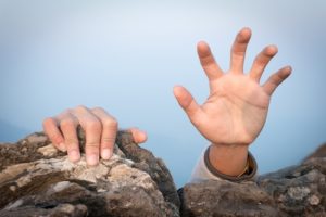 man reaching hand out on cliff