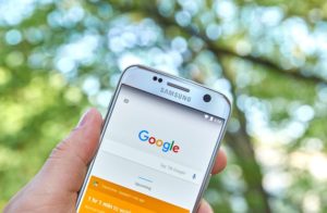 Person standing outside holding up smartphone displaying Google homepage