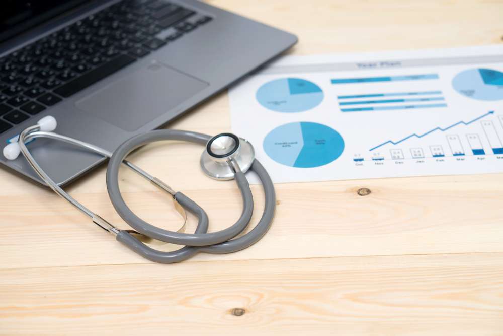 Wooden table with a laptop, stethoscope, and pie chart