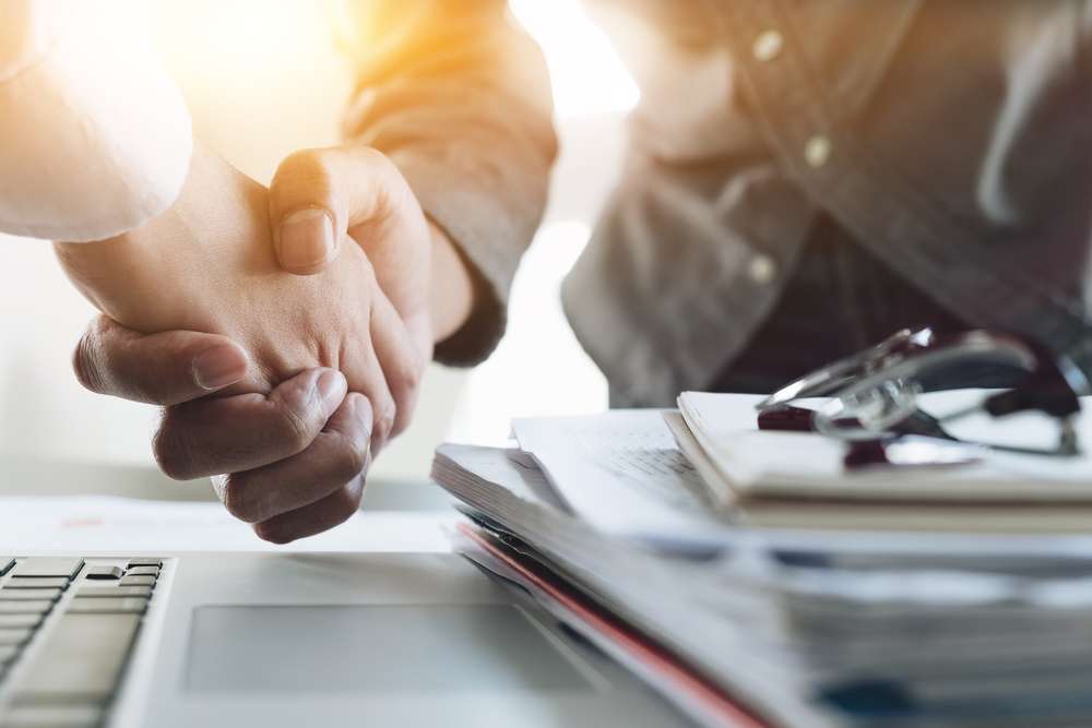 Two people shaking hands over a desk