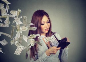 Young woman looking into wallet and watching money fly away