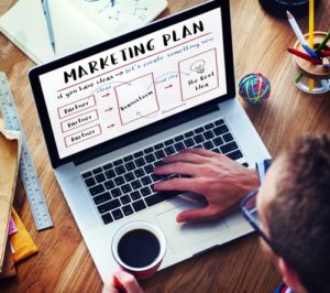 Man drinking coffee looking at laptop displaying marketing plan on screen