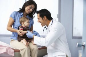 doctor listening to an infant patient's voice and laughing with mother