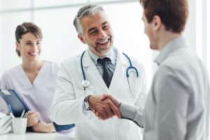 Male doctor shaking hands with male patient while female nurse stands behind them