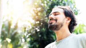 A bearded man is meditating outdoors