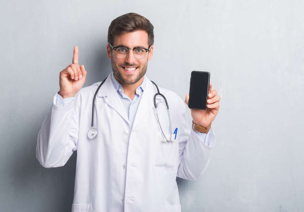 male doctor holding up one finger and a smartphone with the other hand