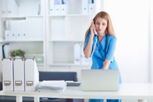 Female nurse looking at laptop while talking on the telephone