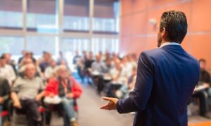 man in suit giving speech to audience at professional referrals symposium