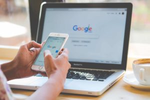 Person using Google on phone while sitting in front of laptop displaying same Google screen