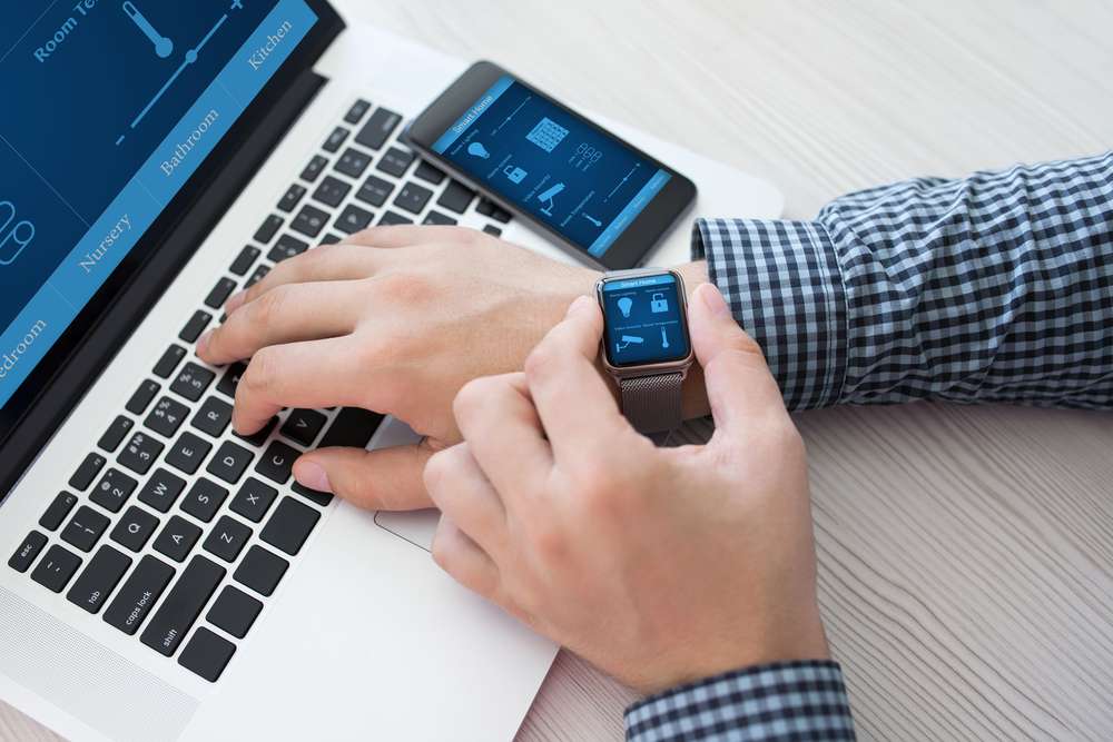 Person sitting in front of their laptop and iPhone, checking their apple watch