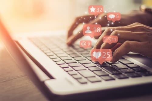 person typing on laptop with holographic social media notifications coming off the keyboard