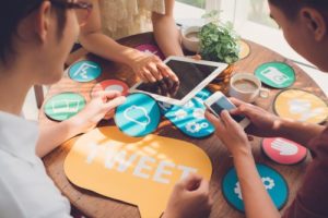 A group of friends sitting together at a small table with tangible social media symbols spread out