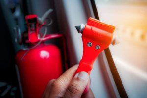 Person holding a fire extinguisher tool used to break glass window