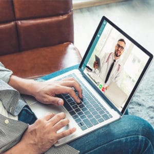 A couple sitting on the sofa with a laptop featuring a telehealth appointment.