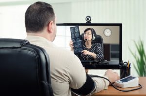 Man getting his blood pressure checked while video chatting with doctor showing x-ray results