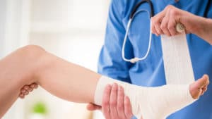 Close-up of male doctor bandaging foot of female patient at doctor's office.