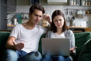 Young couple sitting on a couch looking confused at a laptop