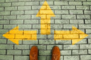 Person's shoes standing before three directional arrows drawn on bricks